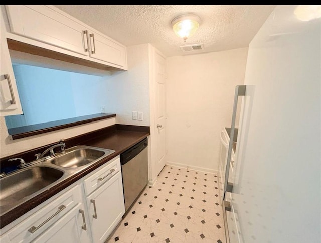 kitchen featuring stainless steel dishwasher, dark countertops, a textured ceiling, light floors, and a sink
