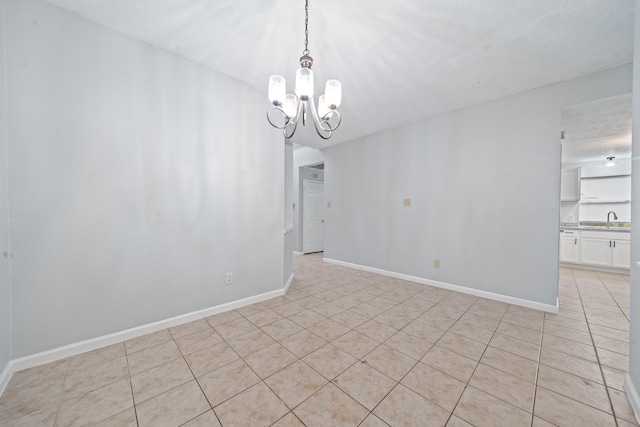 empty room with a chandelier, light tile patterned floors, baseboards, and a sink