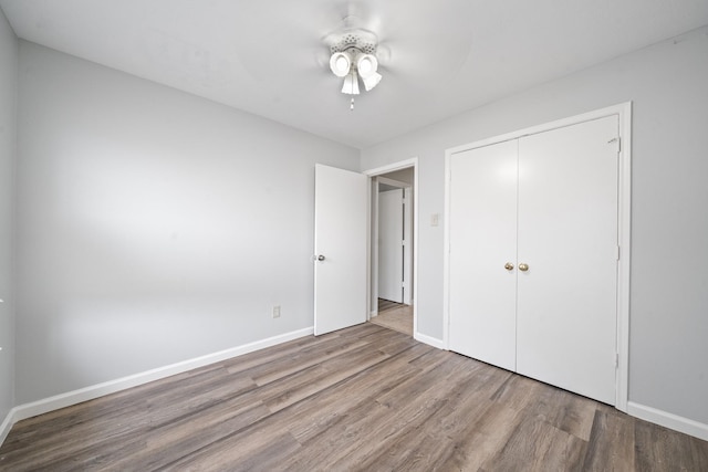 unfurnished bedroom with wood finished floors, a closet, baseboards, and a ceiling fan
