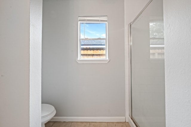 bathroom with tile patterned floors, toilet, a shower with shower door, and baseboards