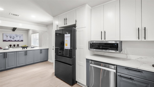 9210 Linkmeadow Ln, Houston, TX 77025 - kitchen featuring stainless steel appliances, gray cabinets, light wood-style floors, white cabinetry, and light stone counters