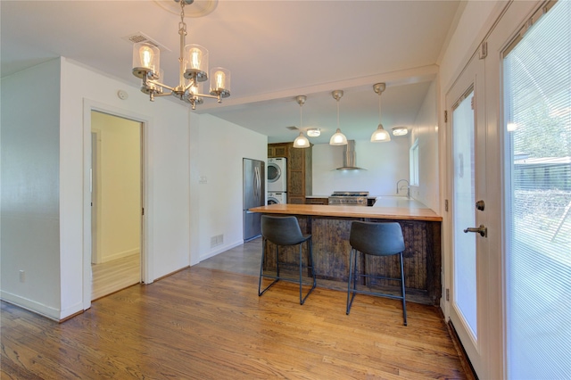 4538 Warm Springs Rd, Houston, TX 77035 - kitchen with stacked washer and clothes dryer, wall chimney exhaust hood, a chandelier, freestanding refrigerator, and stove