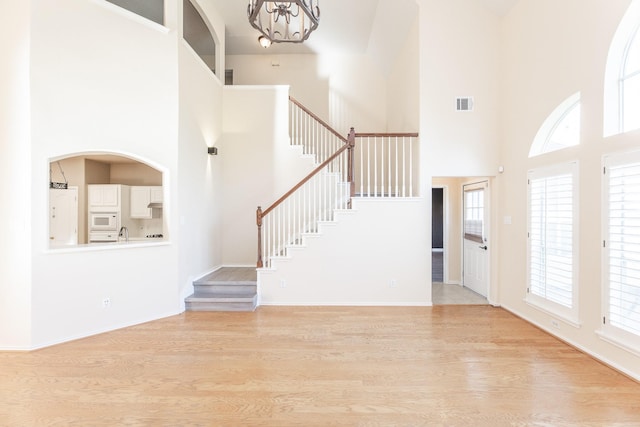 entryway featuring a towering ceiling, a chandelier, stairway, light wood-style flooring, and healthy amount of natural light