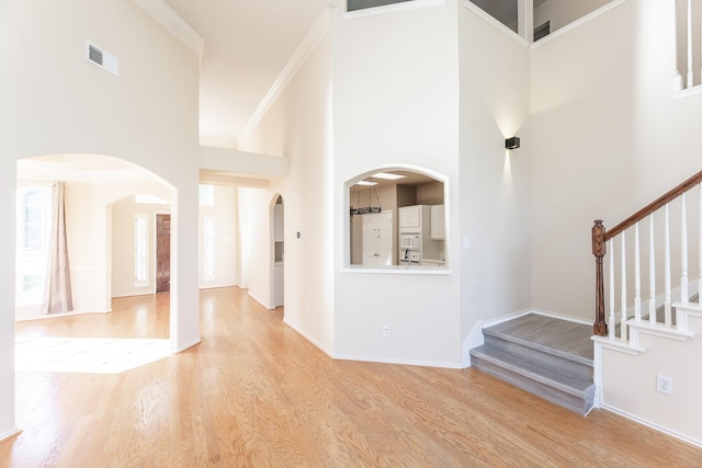 entrance foyer featuring a high ceiling, arched walkways, light wood-type flooring, stairs, and baseboards