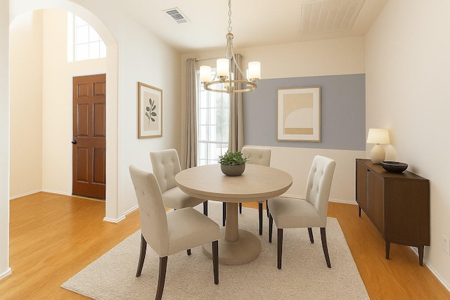 dining space with light wood-type flooring, a chandelier, baseboards, and arched walkways