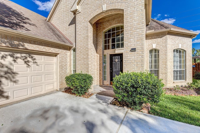 property entrance with brick siding, roof with shingles, concrete driveway, and an attached garage
