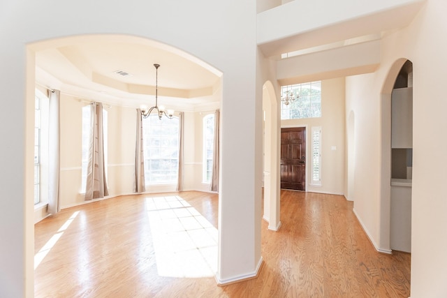 foyer entrance featuring arched walkways, a chandelier, light wood-type flooring, baseboards, and a raised ceiling