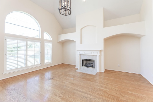 unfurnished living room featuring a chandelier, high vaulted ceiling, a tile fireplace, light wood-style flooring, and arched walkways
