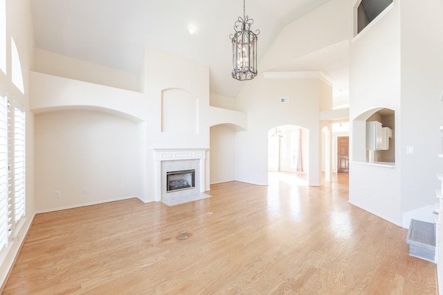 unfurnished living room with high vaulted ceiling, healthy amount of natural light, a fireplace, light wood-style floors, and a chandelier