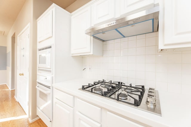 kitchen with under cabinet range hood, white appliances, light wood-style flooring, tasteful backsplash, and white cabinets