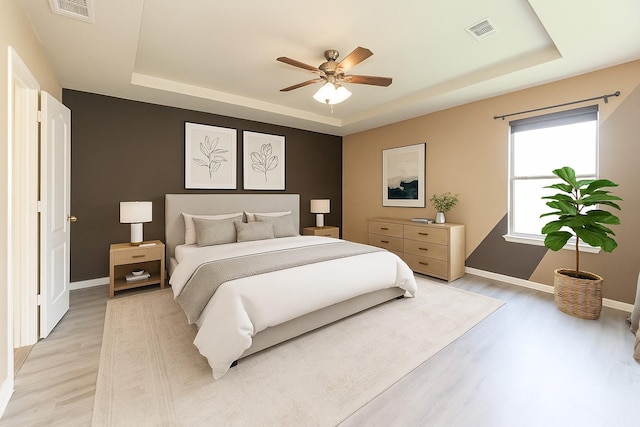 bedroom with a raised ceiling, light wood-style floors, baseboards, and ceiling fan