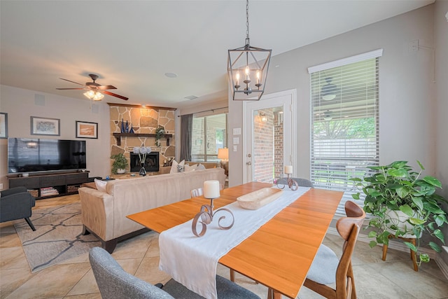 dining room featuring a chandelier, a fireplace, light tile patterned flooring, and ceiling fan