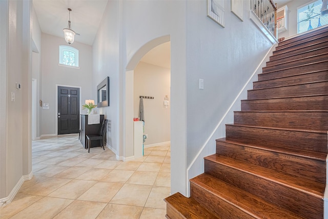 foyer entrance featuring arched walkways, a towering ceiling, stairway, light tile patterned floors, and baseboards