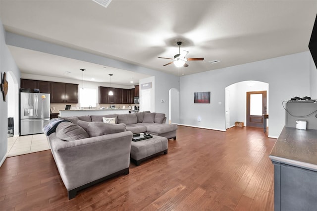 living area featuring arched walkways, a ceiling fan, wood finished floors, and baseboards