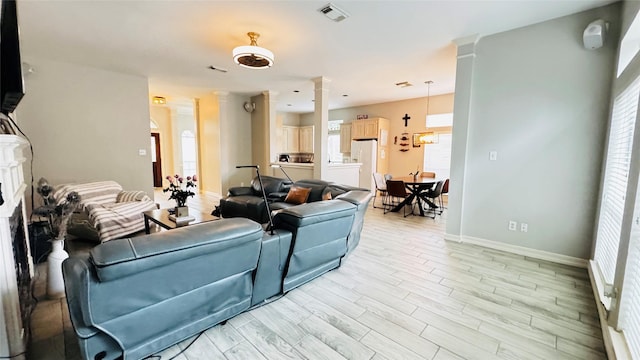 living area featuring plenty of natural light, baseboards, ornate columns, and light wood-type flooring