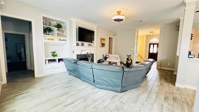 living room featuring light wood finished floors, a large fireplace, decorative columns, baseboards, and built in features