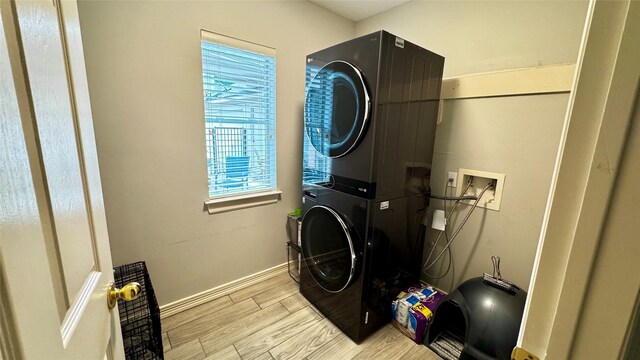clothes washing area with stacked washer / drying machine, baseboards, and light wood-style floors