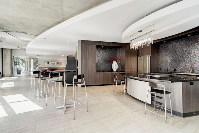 kitchen with built in fridge, stainless steel gas cooktop, a sink, a kitchen bar, and dark brown cabinetry