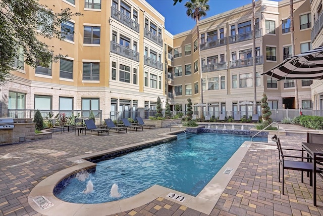 community pool with fence, a patio area, area for grilling, and exterior kitchen