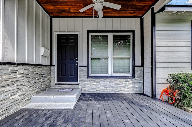 view of exterior entry featuring stone siding, ceiling fan, and a deck