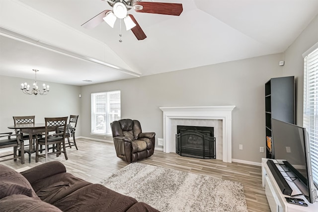 living area featuring ceiling fan, healthy amount of natural light, light wood finished floors, vaulted ceiling, and a chandelier