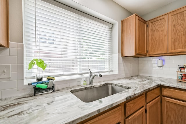 kitchen with a sink, light stone countertops, backsplash, and brown cabinetry