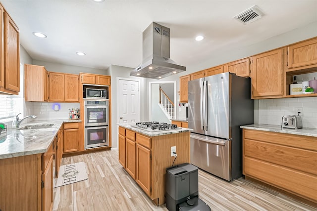 kitchen with appliances with stainless steel finishes, island range hood, backsplash, light wood-style flooring, and light stone countertops