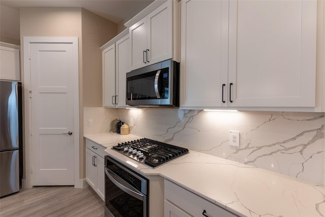 kitchen featuring stainless steel appliances, tasteful backsplash, light wood finished floors, white cabinets, and light stone countertops