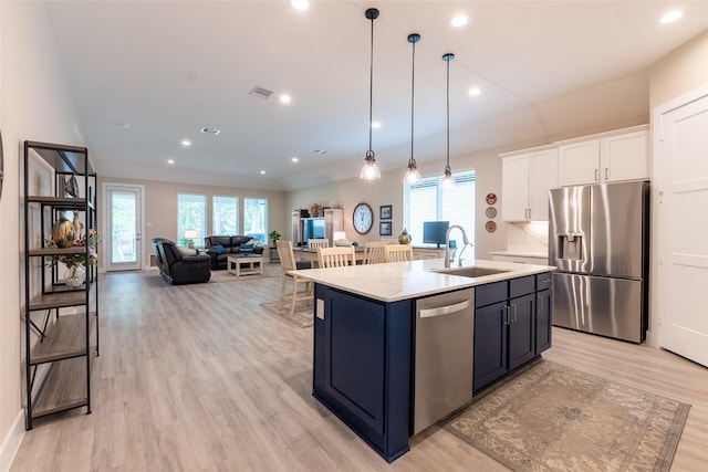 kitchen with stainless steel appliances, a sink, light wood-type flooring, white cabinetry, and an island with sink