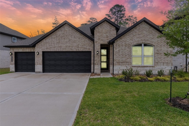 french provincial home featuring brick siding, an attached garage, concrete driveway, a yard, and a shingled roof