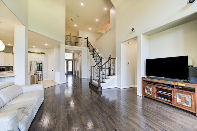 living area featuring a towering ceiling, dark wood-style flooring, stairs, baseboards, and recessed lighting