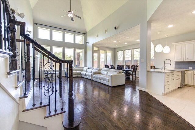 living room featuring ceiling fan, plenty of natural light, stairs, light wood-style floors, and high vaulted ceiling