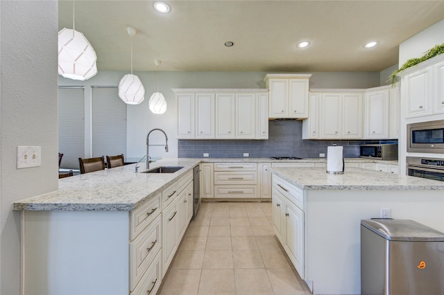 kitchen with a sink, appliances with stainless steel finishes, backsplash, light tile patterned floors, and a peninsula