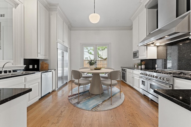 6104 San Felipe St, Houston, TX 77057 - kitchen with wall chimney range hood, built in appliances, a sink, white cabinetry, and ornamental molding