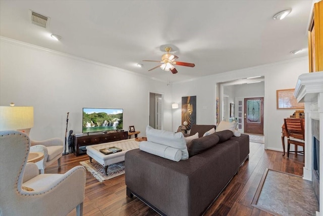 living area featuring a fireplace, ceiling fan, crown molding, and dark wood finished floors