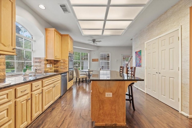 kitchen with light brown cabinetry, stainless steel appliances, a kitchen breakfast bar, dark wood-style floors, and recessed lighting