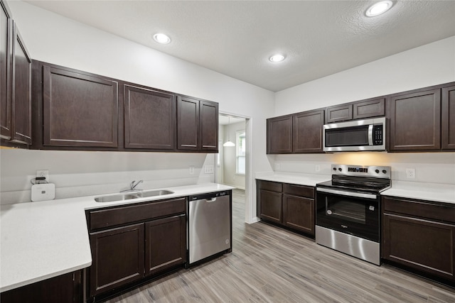 kitchen featuring stainless steel appliances, a sink, dark brown cabinets, light countertops, and recessed lighting