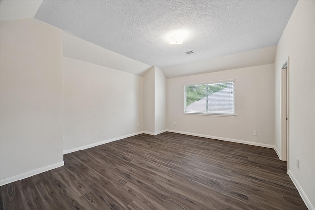 empty room featuring lofted ceiling, dark wood finished floors, a textured ceiling, and baseboards