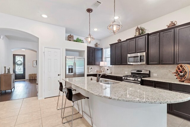 17219 Rookery Ct, Conroe, TX 77385 - kitchen with stainless steel appliances, a sink, arched walkways, dark brown cabinetry, and backsplash