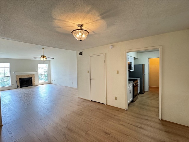 7400 Bellerive Dr Unit 1004, Houston, TX 77036 - unfurnished living room with light wood finished floors, a textured ceiling, a fireplace, and a ceiling fan