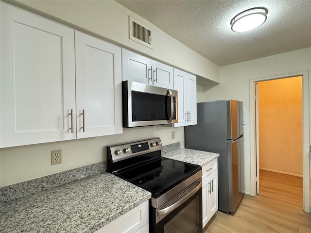 7400 Bellerive Dr Unit 1004, Houston, TX 77036 - kitchen featuring appliances with stainless steel finishes, light wood finished floors, white cabinets, a textured ceiling, and light stone counters