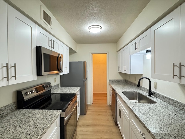 7400 Bellerive Dr Unit 1004, Houston, TX 77036 - kitchen with appliances with stainless steel finishes, a sink, light wood-type flooring, a textured ceiling, and white cabinetry