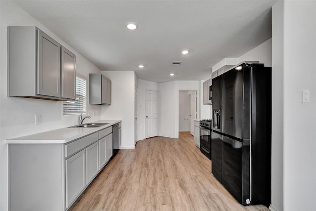 kitchen featuring black appliances, a sink, light wood-type flooring, gray cabinets, and light countertops