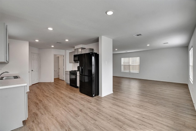 kitchen with black appliances, a sink, light wood-type flooring, light countertops, and baseboards