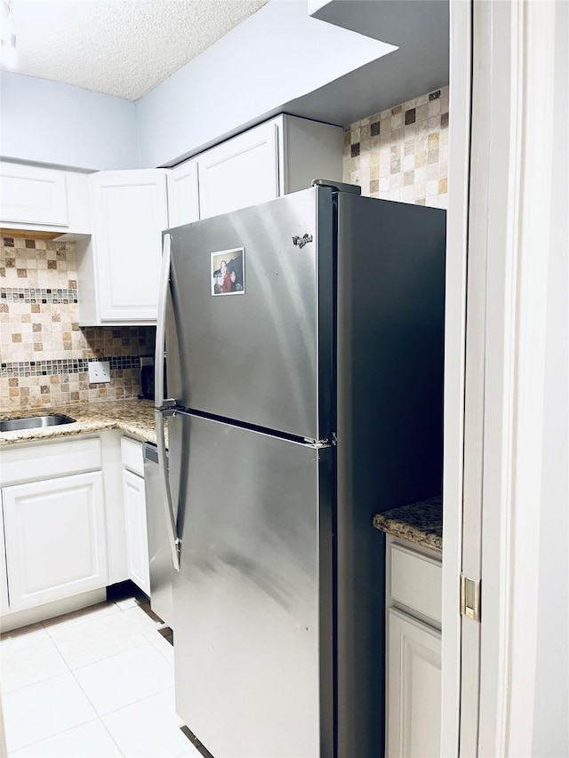 kitchen featuring appliances with stainless steel finishes, white cabinetry, decorative backsplash, light stone countertops, and light tile patterned flooring