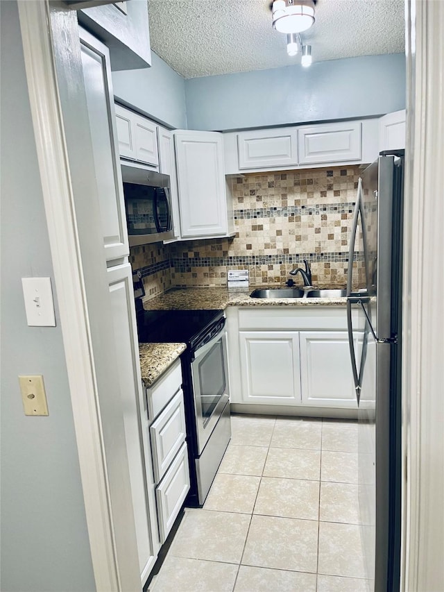 kitchen with appliances with stainless steel finishes, decorative backsplash, a textured ceiling, white cabinetry, and light tile patterned flooring