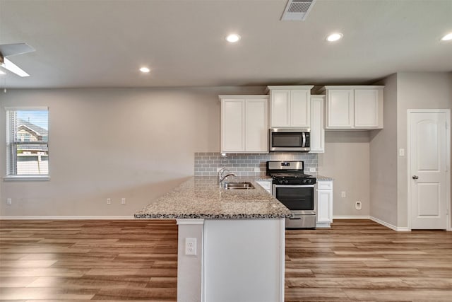 kitchen with stainless steel appliances, a sink, light wood-style floors, white cabinets, and backsplash