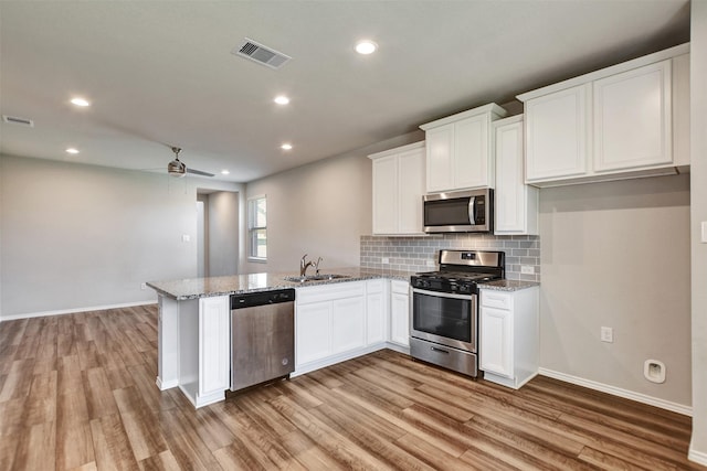 kitchen featuring stainless steel appliances, a sink, a peninsula, white cabinets, and light wood-style floors