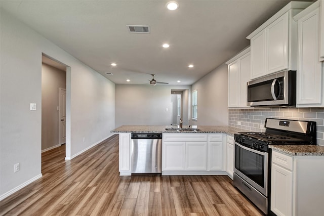 kitchen featuring stainless steel appliances, a sink, a peninsula, light wood-type flooring, and white cabinetry