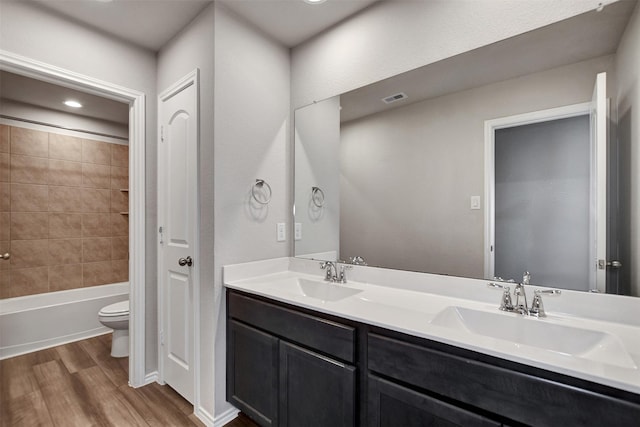 bathroom featuring wood finished floors, toilet, double vanity, and bathing tub / shower combination